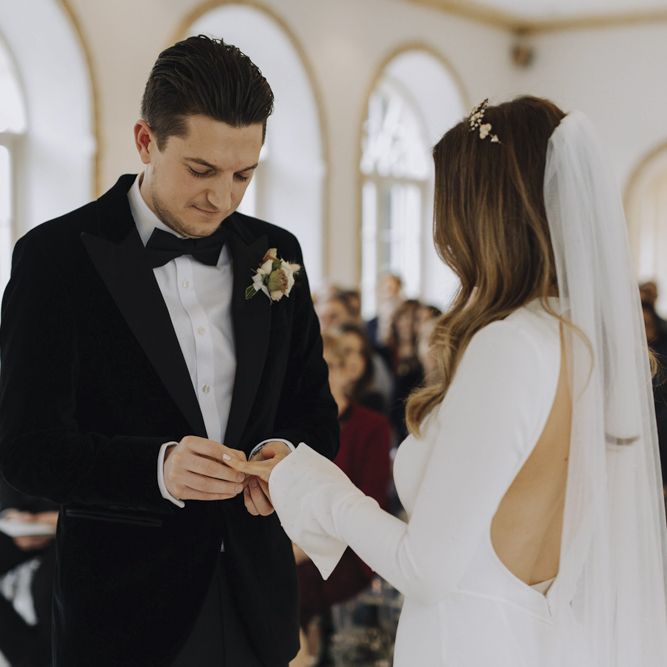 Bride in Emma Beaumont Wedding Dress and Groom in Tuxedo Exchanging Rings