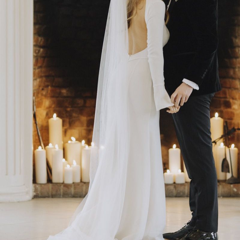 Bride in Backless Emma Beaumont Wedding Dress and Groom in Black Tie Suit Kissing at the Altar
