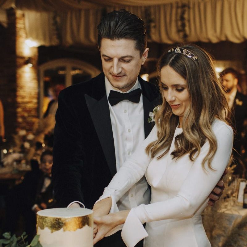 Bride in Emma Beaumont Wedding Dress and Groom in tuxedo Cutting The Wedding Cake
