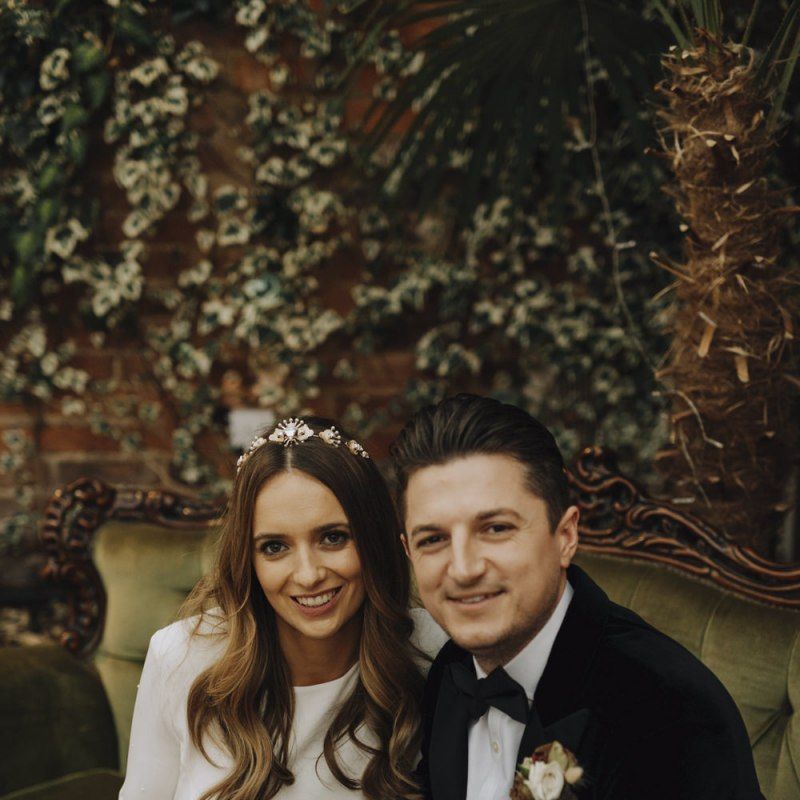 Bride in Emma Beaumont Wedding Dress and Groom in Tuxedo Sitting on an Ornate sofa