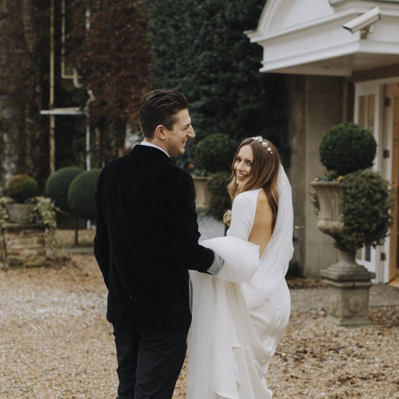 Groom in Black Tie Suit Holding Up Brides Wedding Dress Train and Cathedral Veil