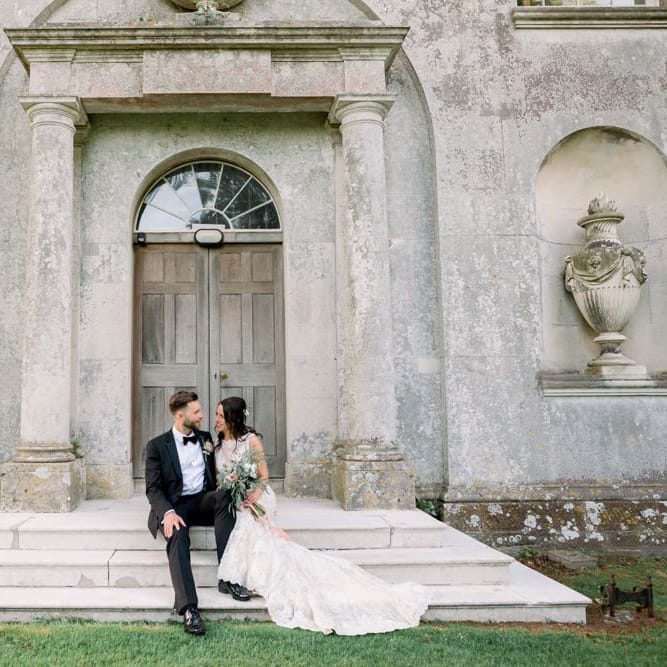 Bride and groom sit on the steps at Lulworth Castle