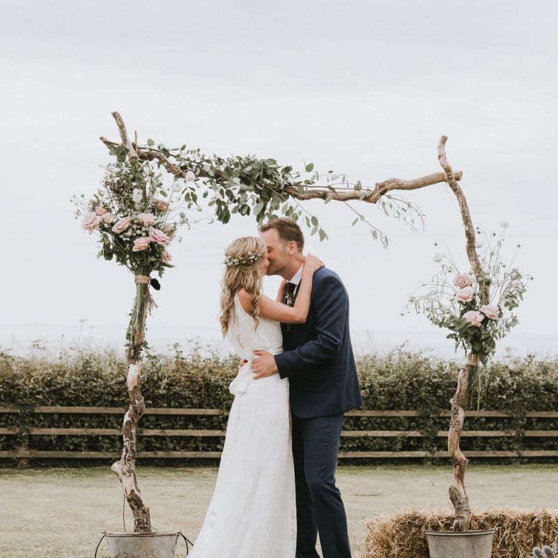 Bride and groom kiss under wooden altar decor