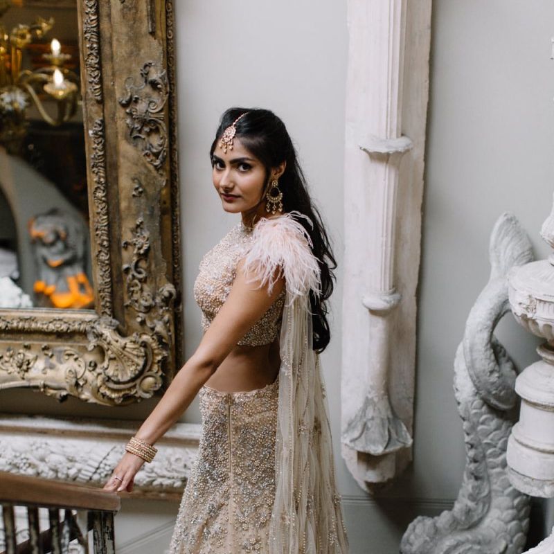 Bride in gold and blush Indian separates with feathers and cape