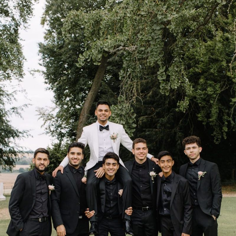 Groomsmen in black shirts and suits and groom in white dinner jacket