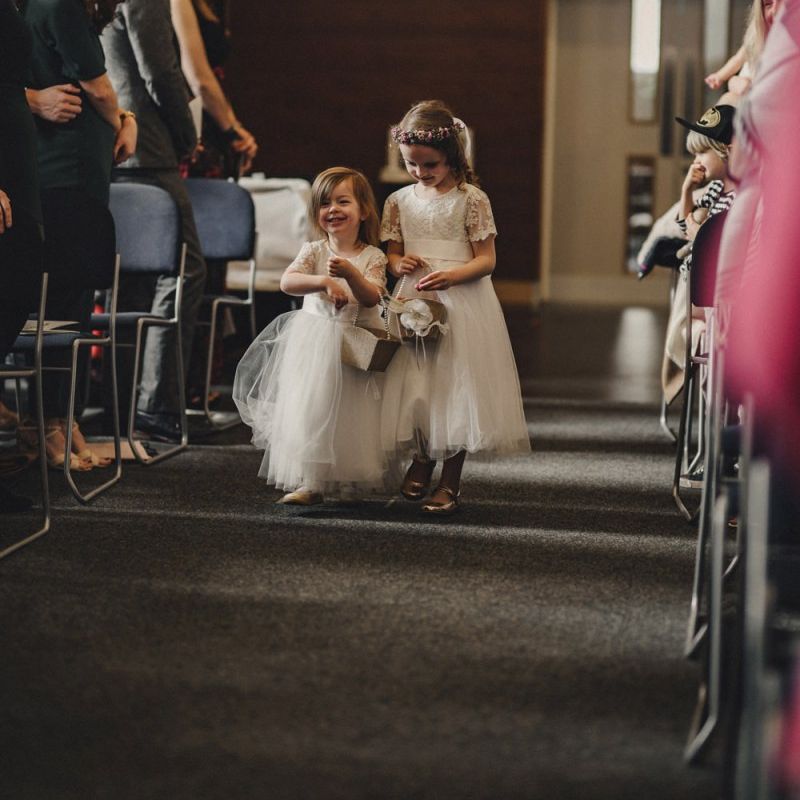 Flower girls in white dresses walking down the aisle