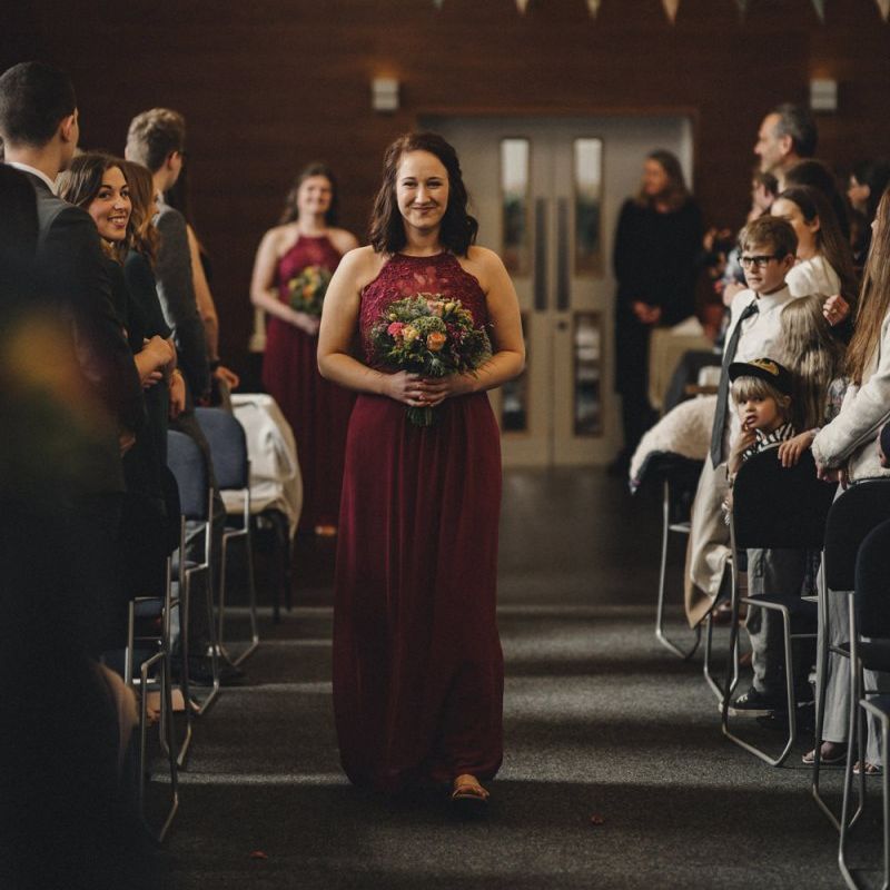 Bridesmaid in red halterneck dress walking down the aisle
