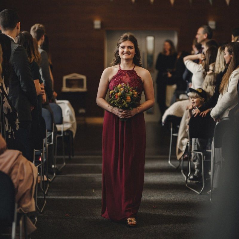 Bridesmaid in red dress walking down the aisle
