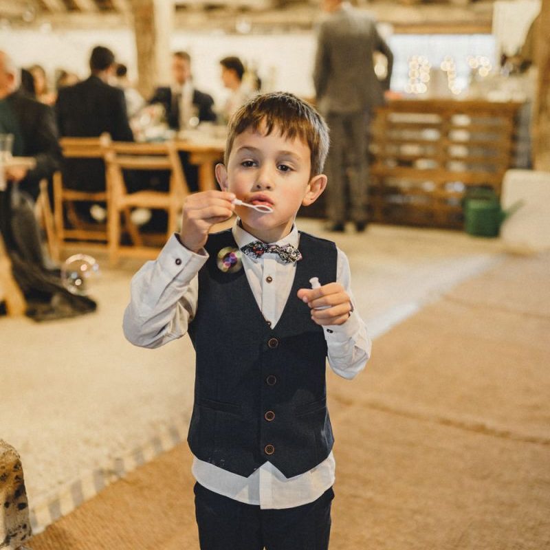 Page boy blowing bubbles at rustic wedding