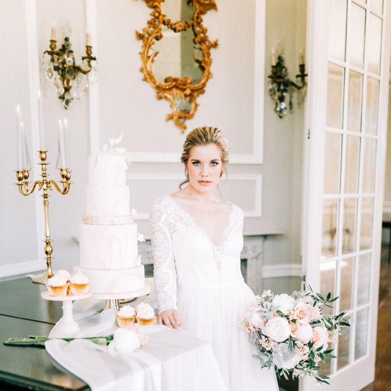 Bride in Lace Wedding Dress Standing Next to Elegant Wedding Cake