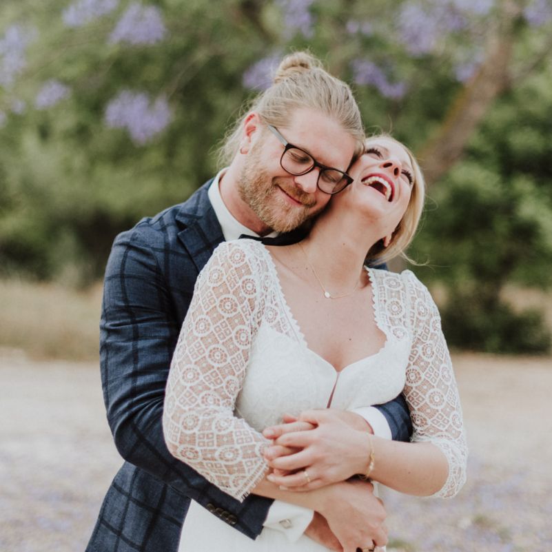 Bride in Rembo Styling Wedding Dress and Groom in Checked Blazer Embracing
