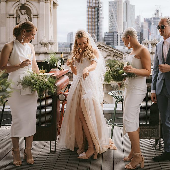 Bridal Party Champagne | Bride in Bespoke Wedding Gown with Blush Underskirt and One Off Shoulder Strap | Fingertip Length Veil Customised with Feathers | Half Up Half Down Bridal Hair | Nude Topshop Shoes with Pom Pom | Bridesmaids in Mismatched White Dresses | Bridesmen in Blue Suits | Homemade Bouquets of White Flowers, Ferns and Foliage | Bike Shed Motorcycle Club Wedding for ELLE Digital Editor | Nigel John Photography