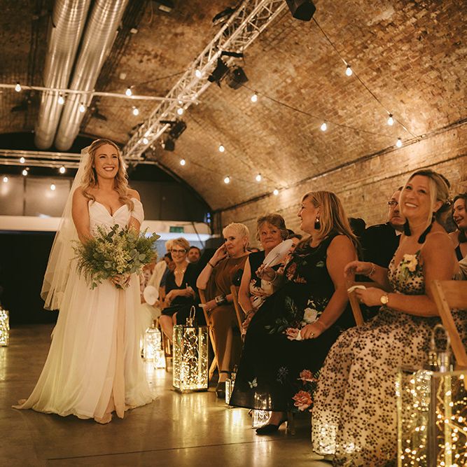 Bride Walking Herself Down Aisle |  Bespoke Wedding Gown with Blush Underskirt and One Off Shoulder Strap | Fingertip Length Veil Customised with Feathers | Half Up Half Down Bridal Hair | Nude Topshop Shoes with Pom Pom | Homemade Bouquet of White Flowers, Ferns and Foliage | Lanterns Filled with Fairylights | Festoon Lights | Bike Shed Motorcycle Club Wedding for ELLE Digital Editor | Nigel John Photography