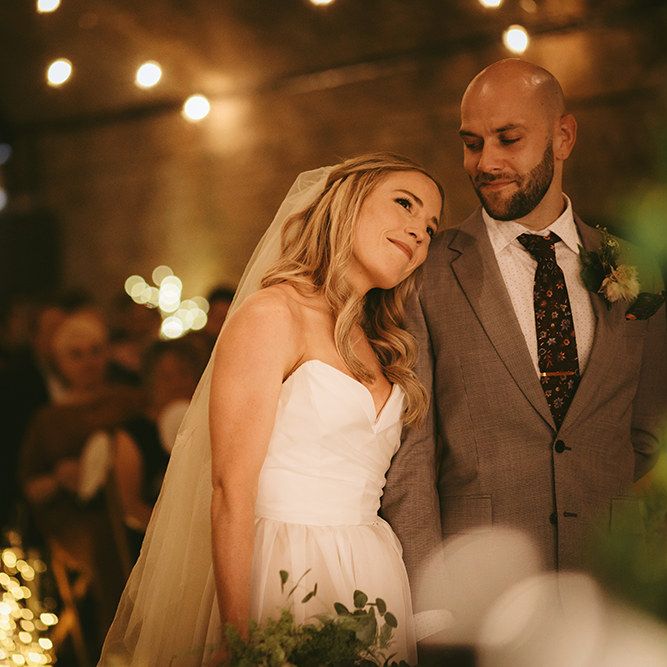 Wedding Ceremony | Bride in  Bespoke Wedding Gown with Blush Underskirt and One Off Shoulder Strap | Fingertip Length Veil Customised with Feathers | Homemade Bouquet of White Flowers, Ferns and Foliage | Groom in Grey Puppy Tooth Check Two-Piece Paul Smith Suit with Amber Tie Pin, Pocket Square and Braces | Bike Shed Motorcycle Club Wedding for ELLE Digital Editor | Nigel John Photography