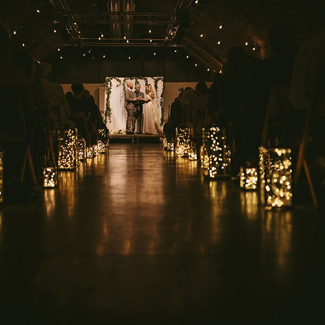 Wedding Ceremony | Bride in  Bespoke Wedding Gown with Blush Underskirt and One Off Shoulder Strap | Fingertip Length Veil Customised with Feathers | Groom in Grey Puppy Tooth Check Two-Piece Paul Smith Suit with Amber Tie Pin, Pocket Square and Braces | Lanterns Filled with Fairylights | Festoon Lights | Bike Shed Motorcycle Club Wedding for ELLE Digital Editor | Nigel John Photography