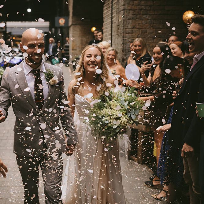 Just Married | Confetti Throw | Bride in Bespoke Wedding Gown with Blush Underskirt and One Off Shoulder Strap | Half Up Half Down Bridal Hair | Homemade Bouquet of White Flowers, Ferns and Foliage | Groom in Grey Puppy Tooth Check Two-Piece Paul Smith Suit with Amber Tie Pin, Pocket Square and Braces | Bike Shed Motorcycle Club Wedding for ELLE Digital Editor | Nigel John Photography