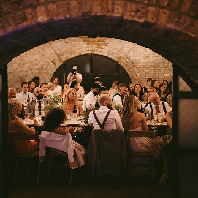 Wedding Reception Speeches | Bride in Bespoke Wedding Gown with Blush Underskirt and One Off Shoulder Strap | Half Up Half Down Bridal Hair | Groom in Grey Puppy Tooth Check Two-Piece Paul Smith Suit with Amber Tie Pin, Pocket Square and Braces | Bike Shed Motorcycle Club Wedding for ELLE Digital Editor | Nigel John Photography