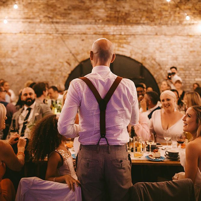 Groom's Speech | Groom in Grey Puppy Tooth Check Two-Piece Paul Smith Suit with Amber Tie Pin, Pocket Square and Braces | Bride in Bespoke Wedding Gown with Blush Underskirt and One Off Shoulder Strap | Half Up Half Down Bridal Hair | Bike Shed Motorcycle Club Wedding for ELLE Digital Editor | Nigel John Photography
