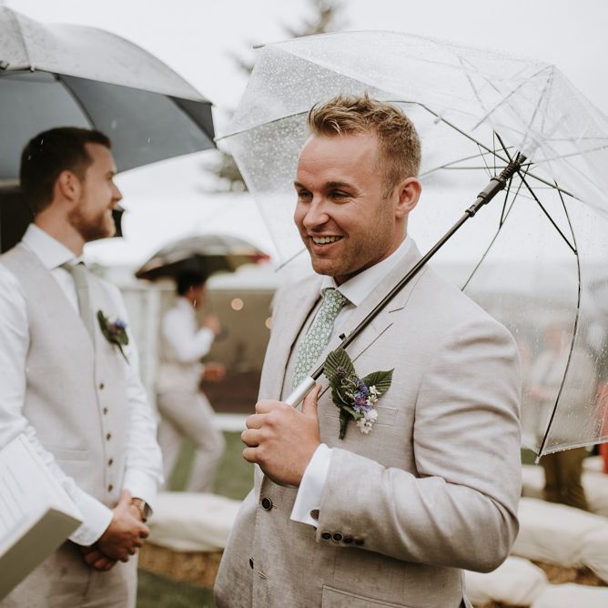 Groom in beige suit under clear umbrella