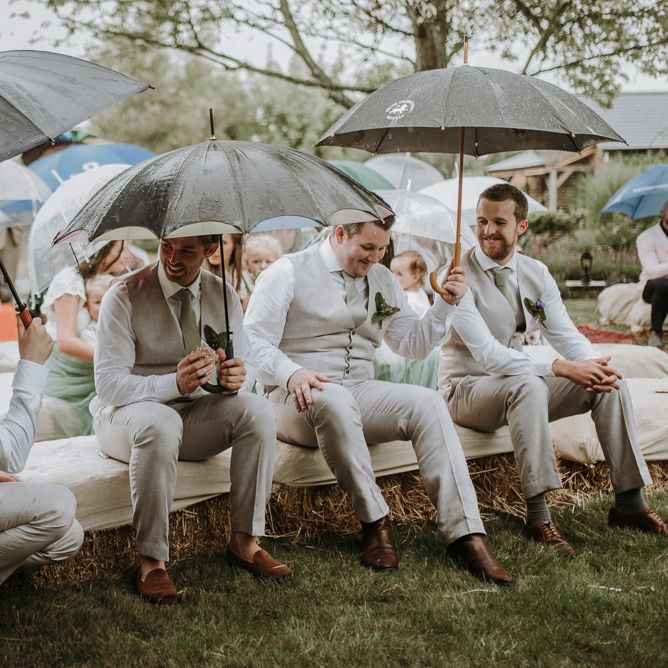 Groomsmen sitting under umbrellas at rainy outdoor garden wedding ceremony