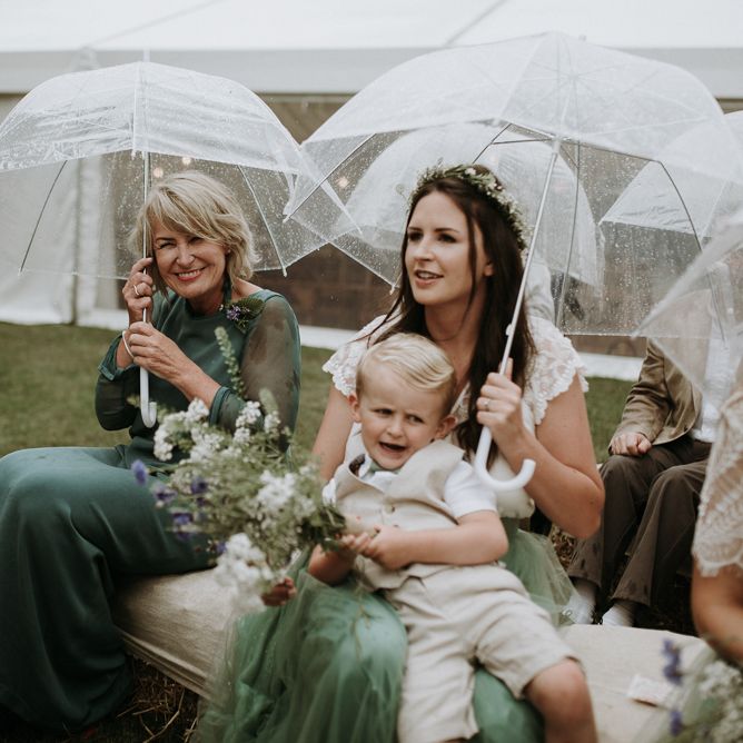 Bridal party sitting under umbrellas at rainy outdoor wedding ceremony
