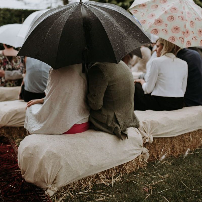 Wedding guests huddled under umbrellas at rainy outdoor wedding