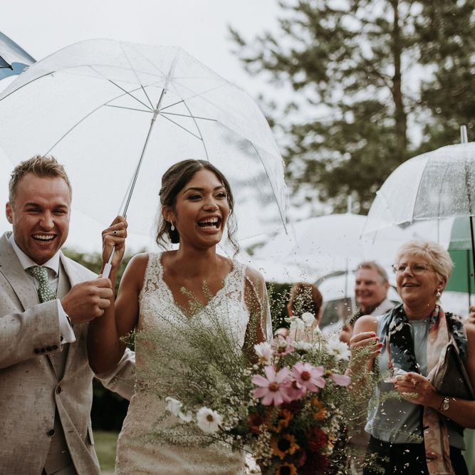 Bride and groom walking up the aisle under umbrellas at garden wedding ceremony