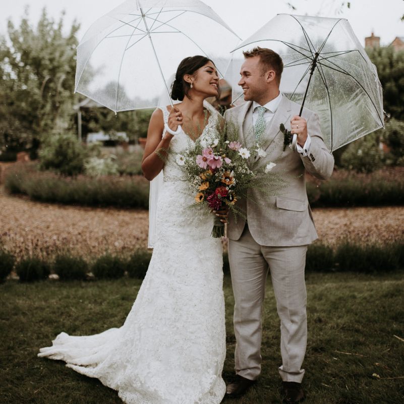 Bride and groom standing under umbrellas after home garden wedding ceremony