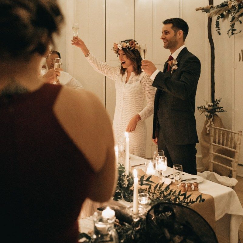 Bride and groom toast at intimate reception with boho floral decor and festoon lighting