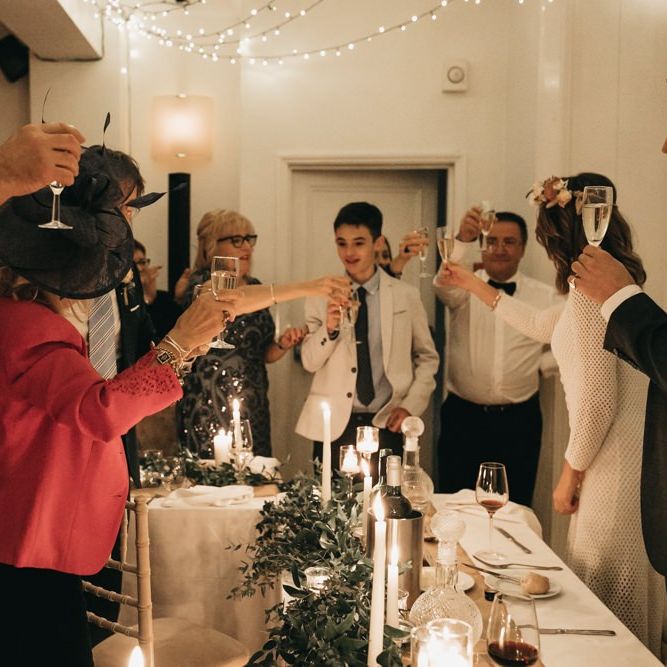 Bride and groom toast with their guests at intimate reception with foliage table decor and taper candles