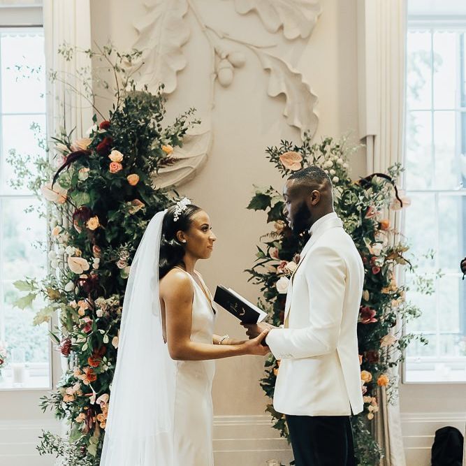 Groom in white tuxedo jacket reading his vows