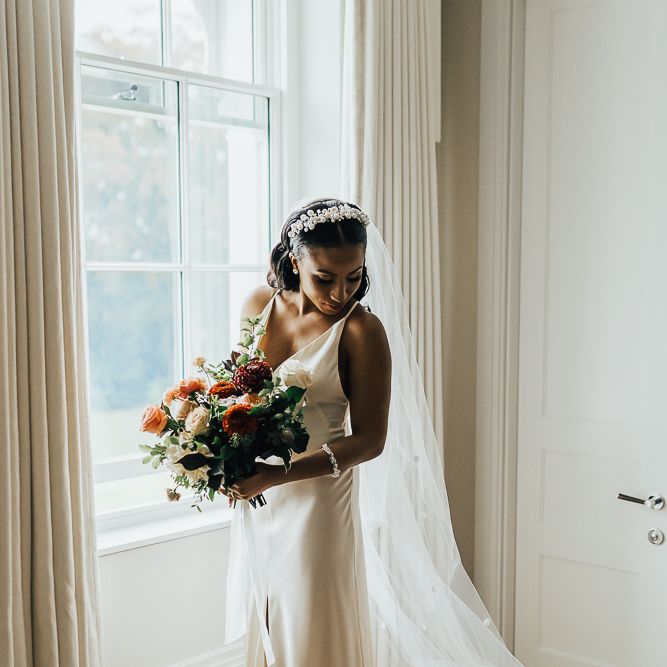 Beautiful bride in slip wedding dress holding her bouquet on the wedding morning