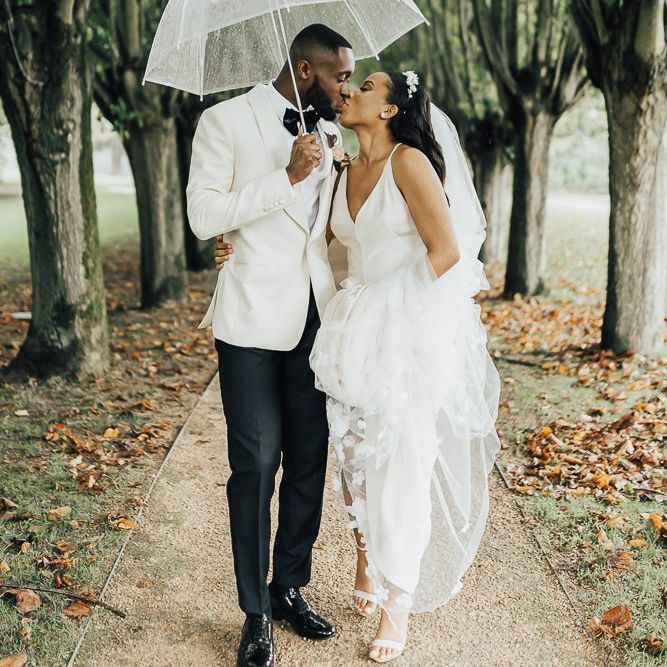 Bride and groom kissing under an umbrella at Coworth Park wedding