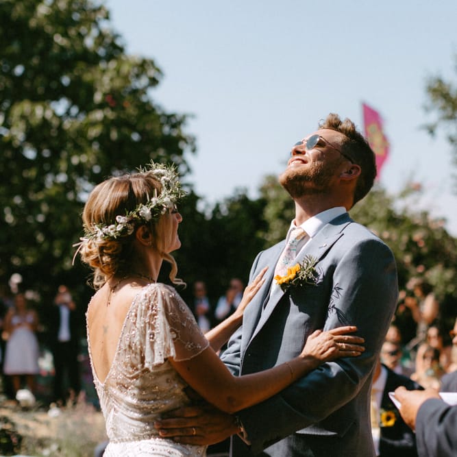Bride in Jenny Packham Portia Wedding Dress and Groom in Grey Ted Baker Suit Laughing at Outdoor Wedding Ceremony