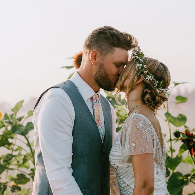 Bride in Jenny Packham Portia Wedding Dress and Flower Crown and Groom in Ted Baker Suit Kissing in a Sunflower Field