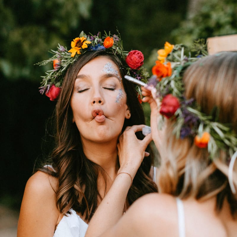 Bridesmaid in White Dress and Colourful Flower Crown putting on Face Glitter
