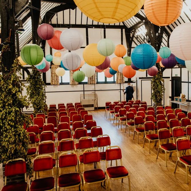 Colourful hanging lanterns at village hall wedding with bright dahlia floral decor
