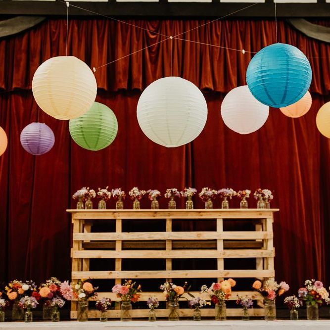 Brightly coloured hanging lanterns at village hall wedding with wooden display and floral decor