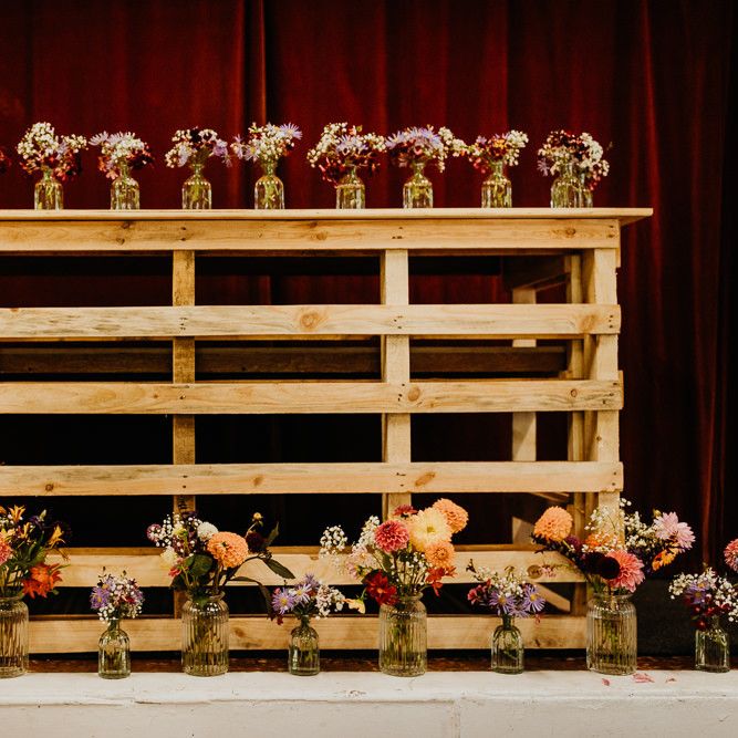Brightly coloured dahlia decor on wooden display at village hall wedding