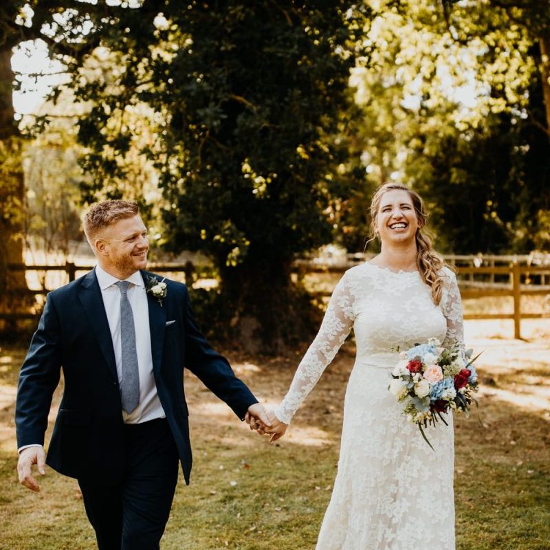 Bride and groom steal a moment at village hall wedding wearing laced long sleeve dress and bright floral bouquet
