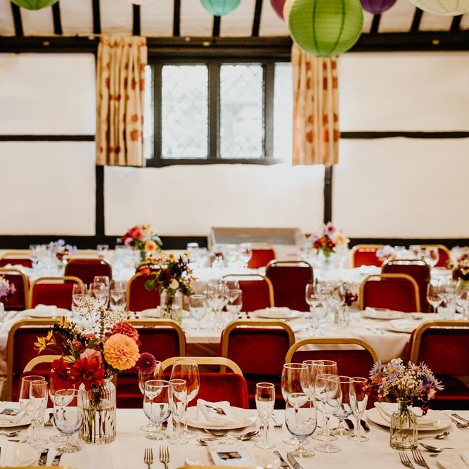 Village hall wedding reception with floral table arrangements of colourful dahlias and hanging lanterns