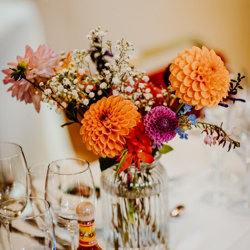 Brightly coloured floral table arrangements of dahlias and gypsophila with hanging lanterns