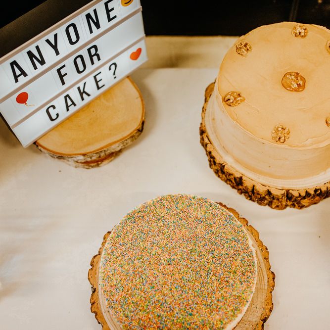 Wedding cakes displayed on rustic styled tree stumps at village hall wedding with hanging lanterns