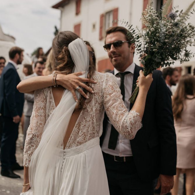 Bride in Donatelle Godart Wedding Dress with Lace V Back and Long Sleeves Hugging Guests