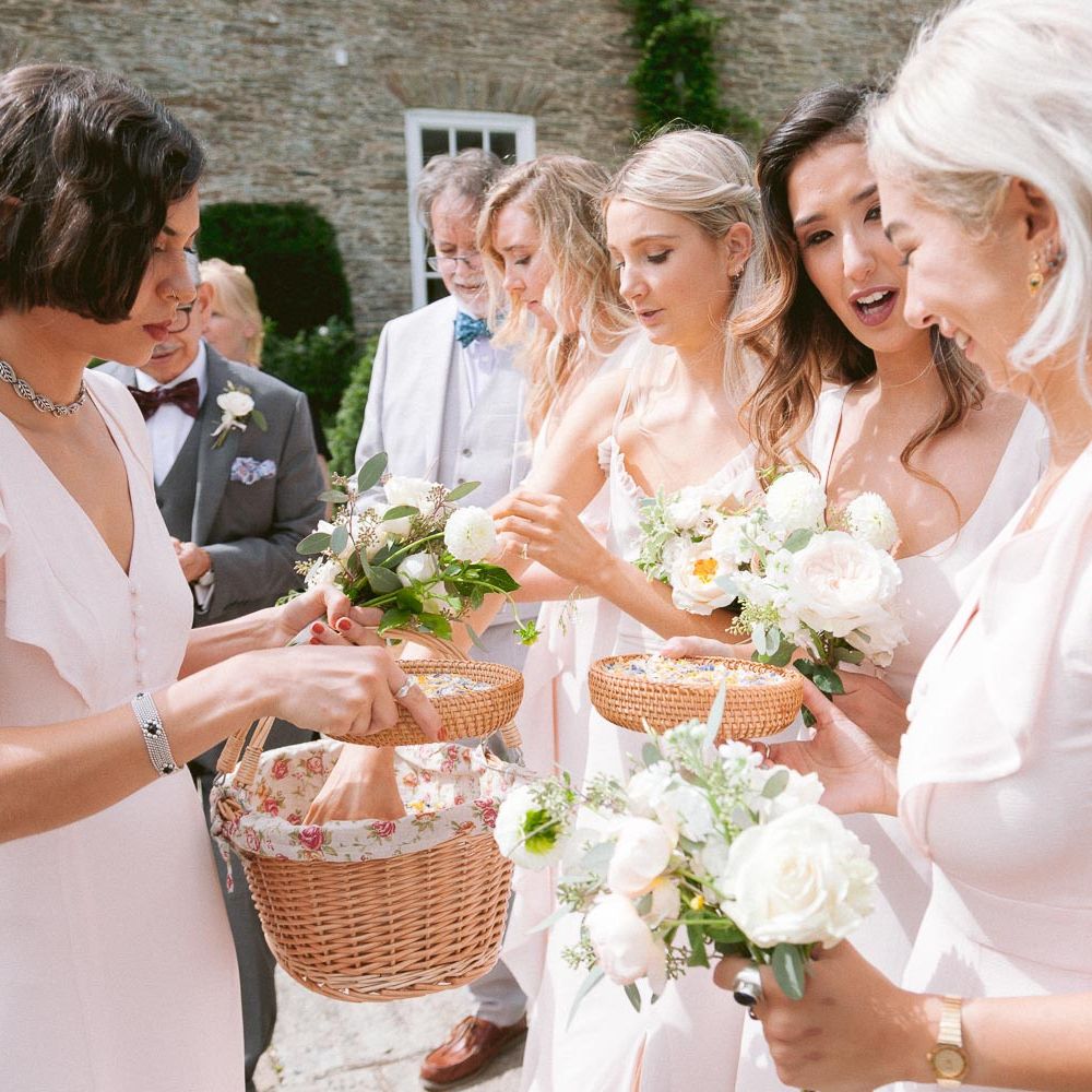 Bridesmaids in blush dresses take confetti from basket