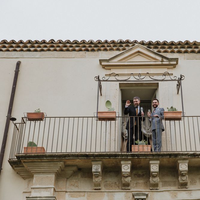 Grooms wave to guests on balcony of Sicilian wedding venue