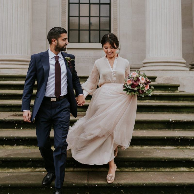 Bride and groom walking down the steps at The Old Marylebone Town Hall in a tulle skirt and navy suit