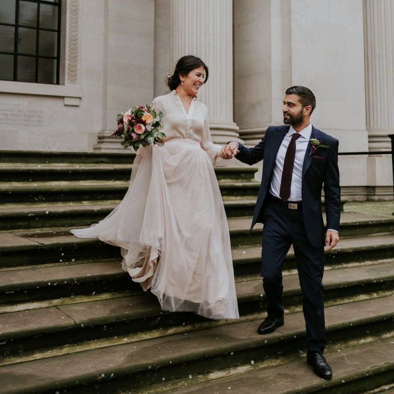Groom helping his bride down the Old Marylebone Town Hall steps in her tulle skirt