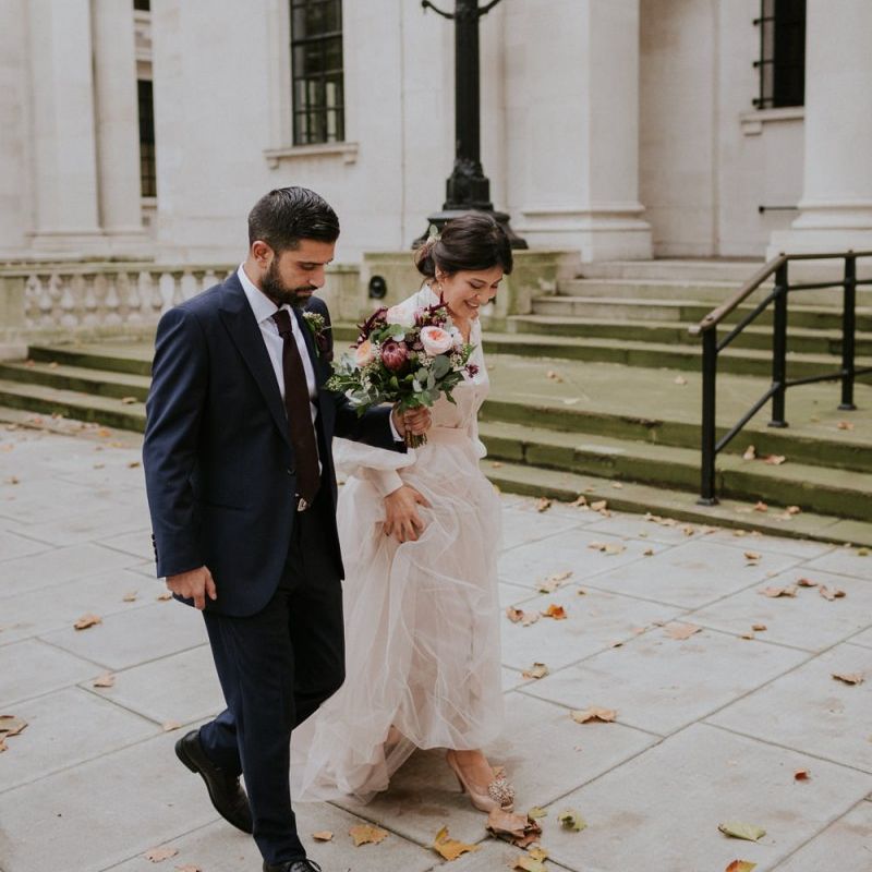 Bride and groom walking through London with autumn leaves on the floor