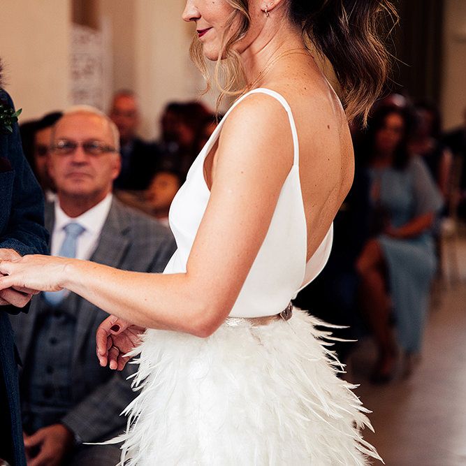 Bride in Charlie Brear Payton Bridal Gown &amp; Piora Feather Skirt and Groom in Three Piece Wool Suit Exchanging Vows